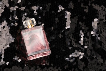 Luxury perfume in bottle on fabric with shiny sequins, above view