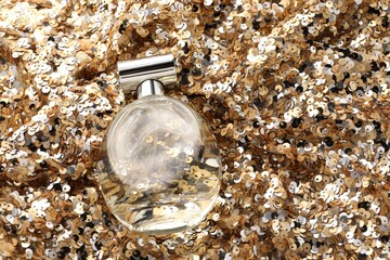 Luxury perfume in bottle on fabric with golden sequins, above view