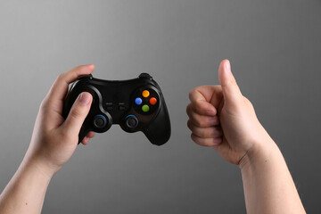 Fototapeta premium Woman using wireless game controller and showing thumbs up on grey background, closeup