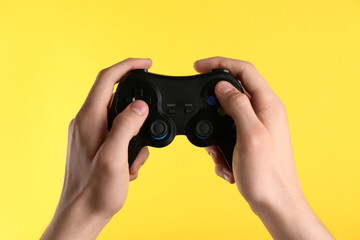 Man using wireless game controller on yellow background, closeup