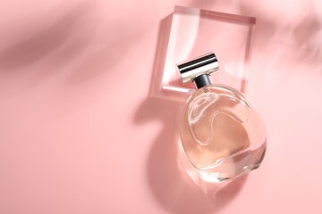 Bottle of luxury women's perfume in sunlight on pink background, top view. Space for text