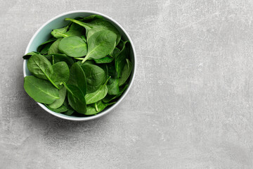 Fresh spinach leaves in bowl on light textured table, top view. Space for text