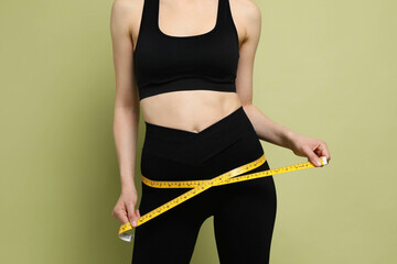 Woman with measuring tape showing her slim body on green background, closeup
