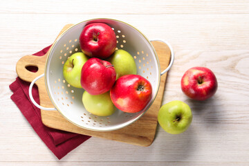 Fresh apples in colander on white wooden table, flat lay