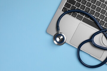 Laptop and stethoscope on light blue background, flat lay. Space for text