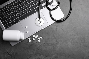 Laptop, stethoscope, pills and bottle on grey table, flat lay. Space for text