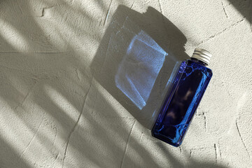 Cosmetic product in blue bottle on light textured background, top view. Space for text