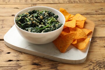Tasty spinach dip with eggs in bowl and nachos chips on wooden table