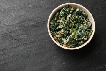 Tasty spinach dip with egg in bowl on black table, top view. Space for text