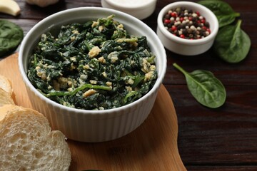 Tasty spinach dip with egg in bowl, bread and spices on wooden table, closeup