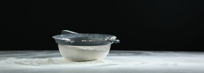 Sieve with flour on table against black background, space for text