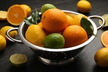 Fresh citrus fruits in colander on dark table, closeup