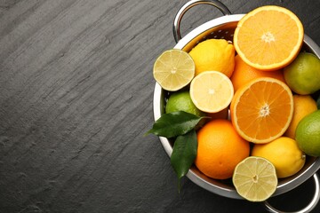 Fresh citrus fruits in colander on dark textured table, top view. Space for text