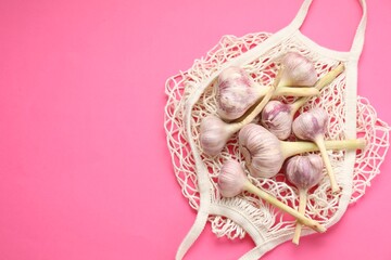 String bag with garlic heads on bright pink background, top view. Space for text