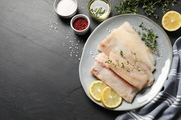 Plate with raw cod fish, microgreens, spices and lemon on dark textured table, flat lay. Space for text