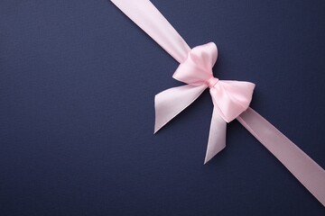 Pink satin ribbon with bow on blue background, top view. Space for text