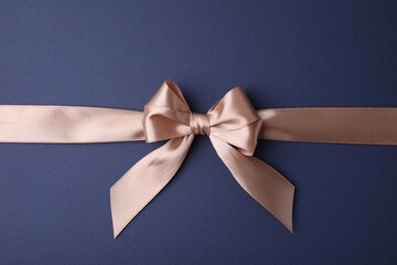Beige satin ribbon with bow on blue background, top view