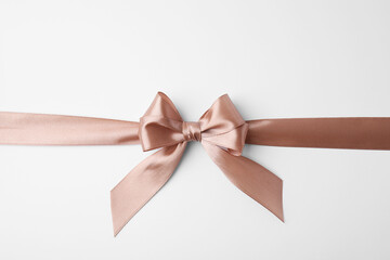 Beige satin ribbon with bow on white background, top view