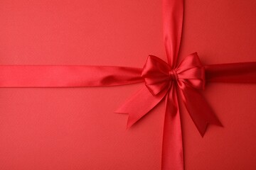 Bright satin ribbon with bow on red background, top view