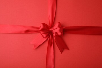 Bright satin ribbon with bow on red background, top view