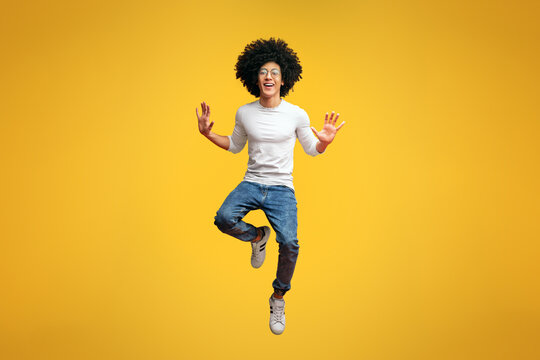 Cheerful millennial guy fooling, jumping in air on orange studio background