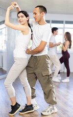 Fototapeta premium Young couple performs an expressive salsa in bright, modern dance studio during a group class