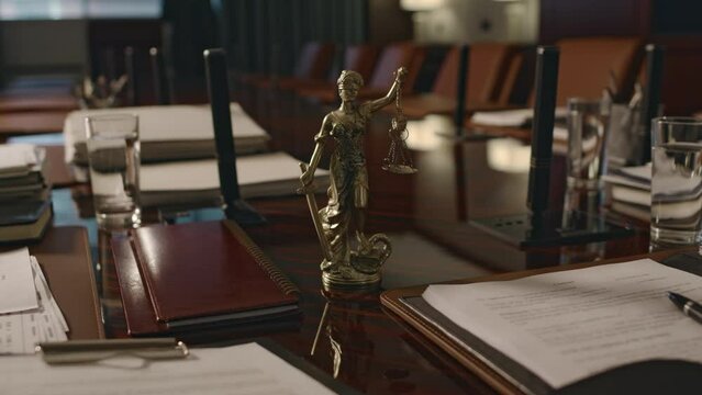 No people footage of bronze statuette of Justitia with scales and sword among documents on wooden conference table in boardroom