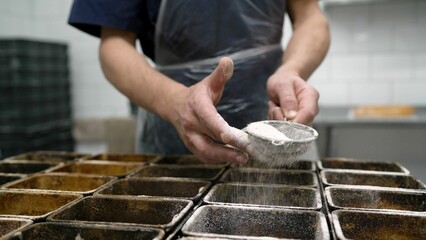 A man sprinkles flour on dough at a kitchen table, close-up. Chef's hands sprinkle bread with...
