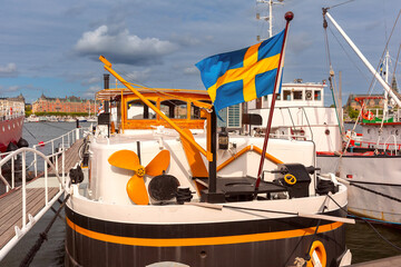 A grand Swedish flag flutters on a boat in a bustling Stockholm harbor, Sweden