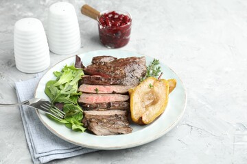 Delicious roasted beef meat, caramelized pear and greens served on light textured table. Space for...