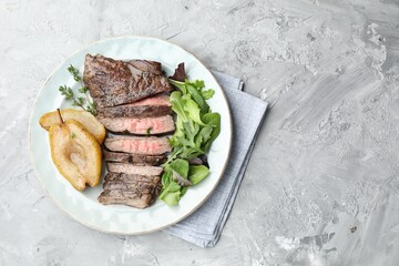Delicious roasted beef meat, caramelized pear and greens on light textured table, top view. Space...