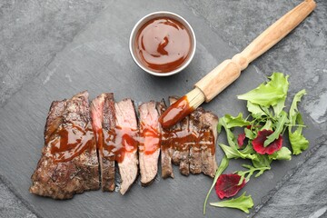 Pieces of delicious roasted beef meat with sauce and greens on black table, top view