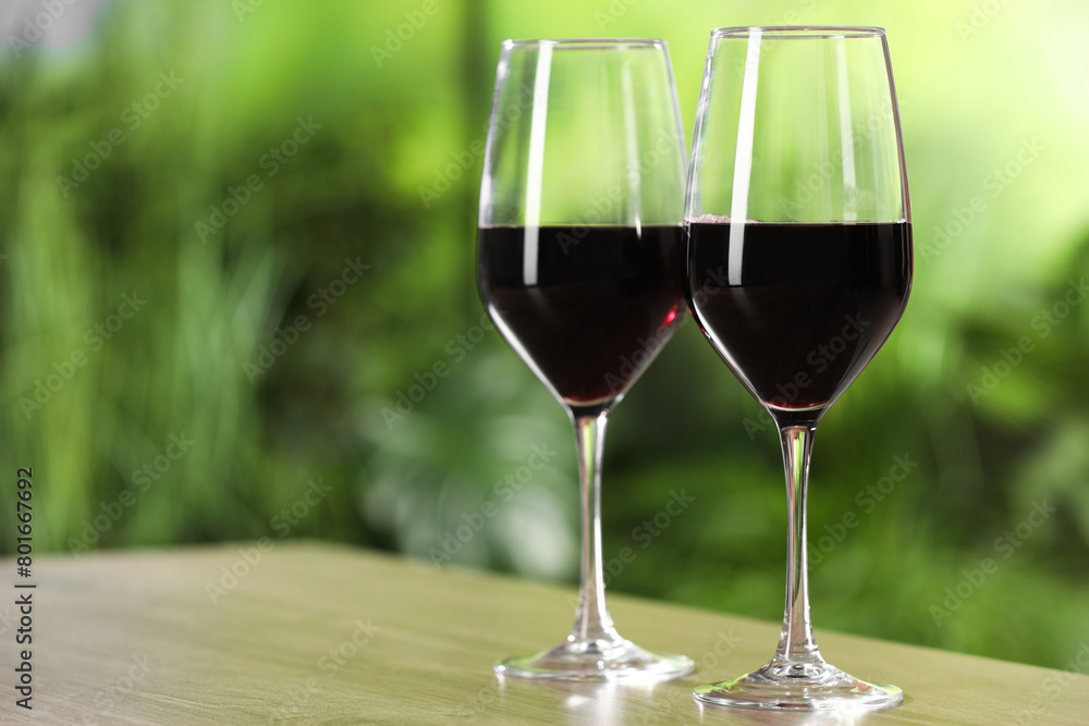 Poster Tasty red wine in glasses on wooden table, space for text