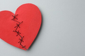 Broken heart. Torn red paper heart sewed with thread on light grey background, top view. Space for...