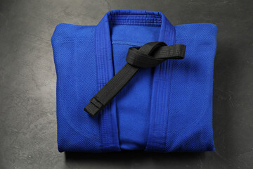 Black karate belt and blue kimono on gray background, top view