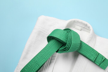 Green karate belt and white kimono on light blue background, top view
