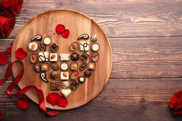 Heart made with delicious chocolate candies and rose petals on wooden table, top view. Space for...