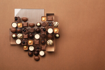 Heart made with delicious chocolate candies on brown background, top view. Space for text