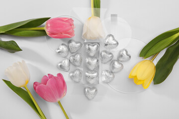 Heart made with delicious chocolate candies and beautiful tulips on white background, top view