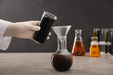 Woman pouring black crude oil from beaker into flask at grey table, closeup