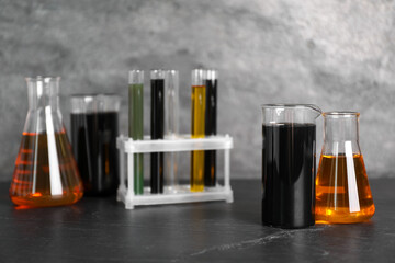 Beakers, flasks and test tubes with different types of oil on grey textured table, closeup