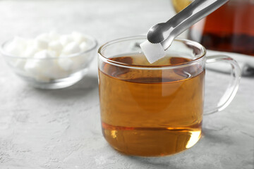 Adding sugar cube into cup of tea at grey textured table, closeup