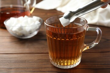 Adding sugar cube into cup of tea at wooden table, closeup