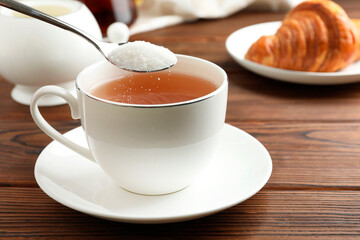 Adding sugar into cup of tea at wooden table, closeup