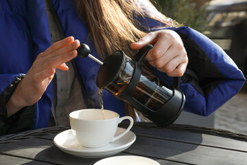 Woman pouring tea into cup at black wooden table in outdoor cafe, closeup