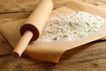 Parchment with flour and rolling pin on wooden table, closeup