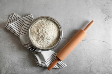 Flour in bowl, rolling pin and napkin on grey table, top view