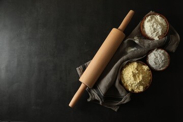 Rolling pin and different types of flour on black table, top view. Space for text