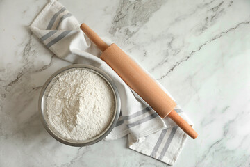 Flour in bowl, rolling pin and napkin on white marble table, top view. Space for text