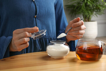 Woman adding sugar into aromatic tea at wooden table indoors, closeup